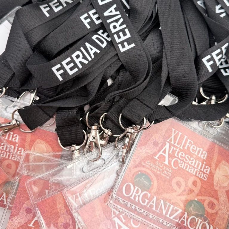 Landyard negros con la inscripción "FERIA DE ARTESANÍA" y credenciales de eventos en fondo rojo.