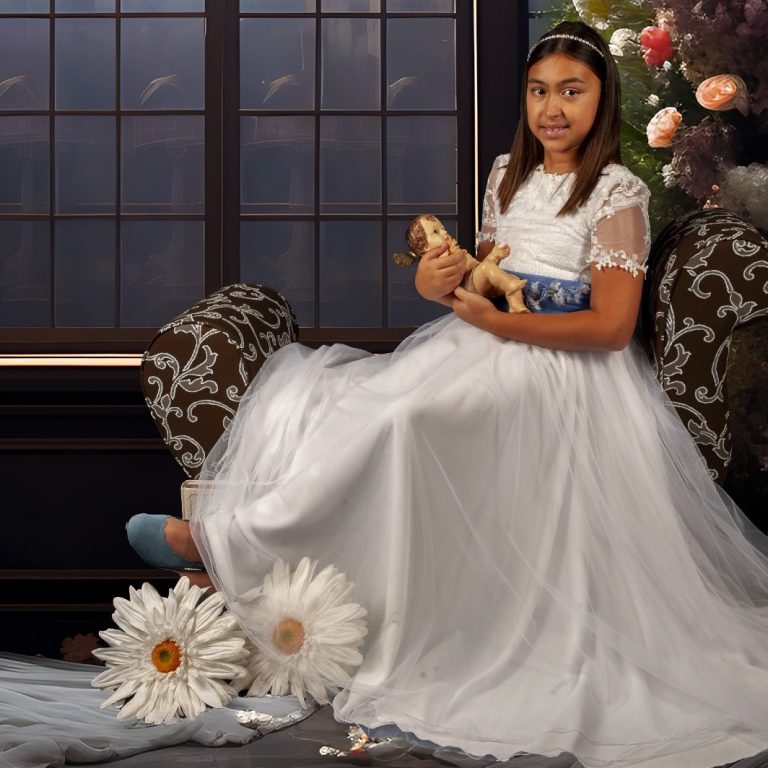 Niña sentada en un sofá, vestida con un vestido blanco de comunión y flores alrededor.